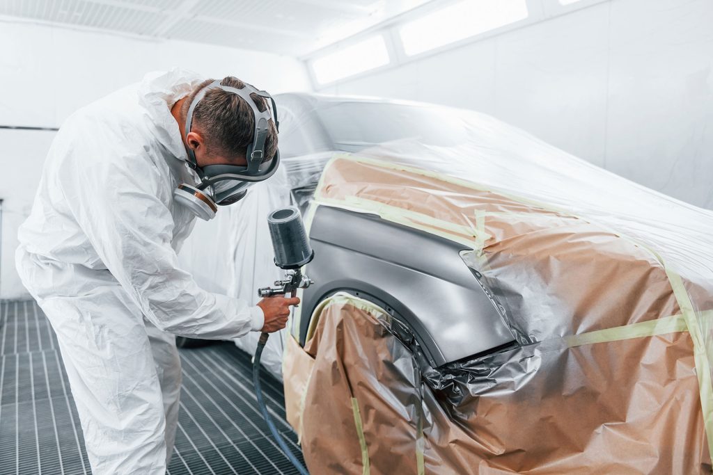 A man painting car in painting booth with spray gun